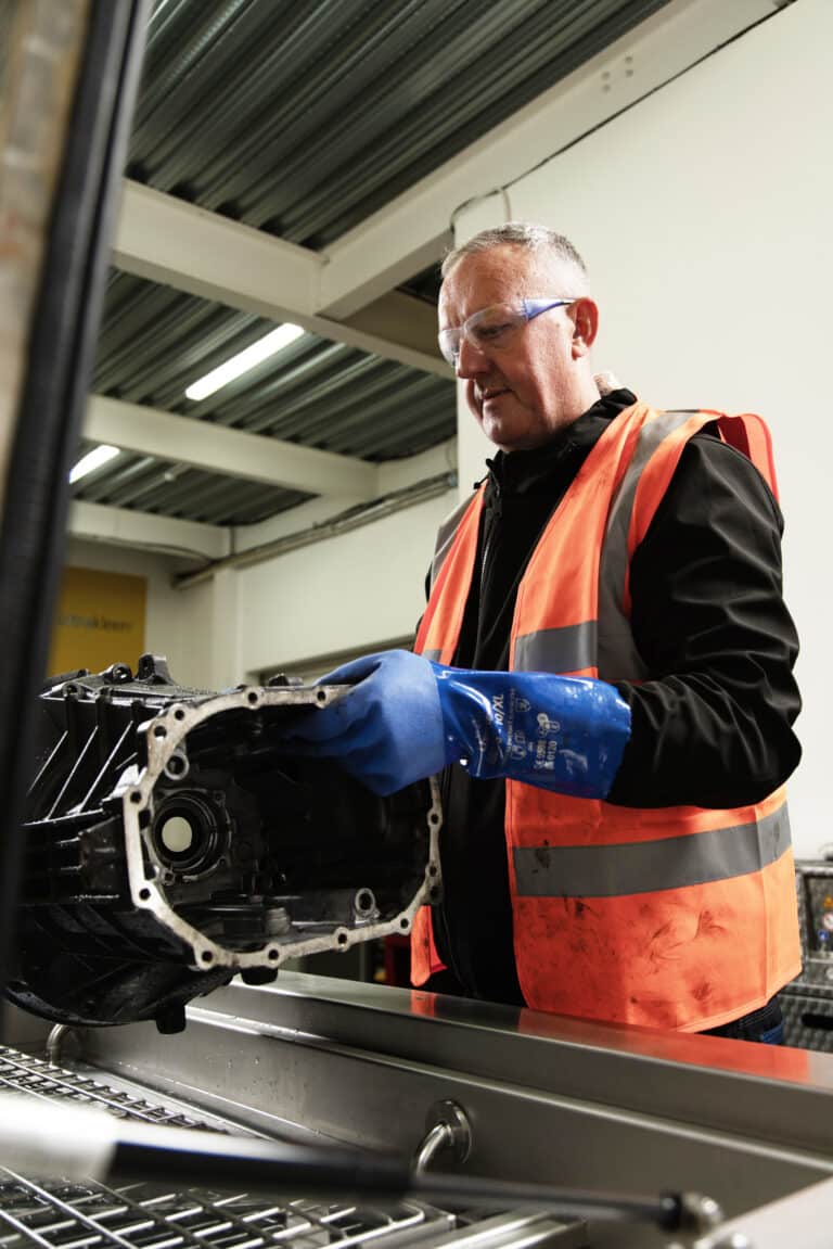 Man lowering a large machine parts into a Ultrasonic parts cleaner for washing