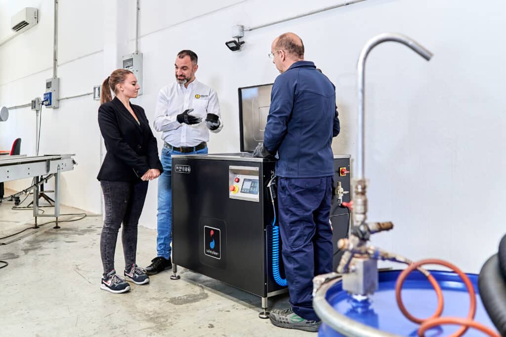 Un técnico experto de Safetykleen demuestra cómo la máquina automática de ultrasonidos SonicKleen de Safetykleen a dos clientes interesados del sector industrial.